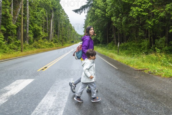 Mother and son crossing a paved road through lush rainforest in ucluelet, vancouver island, emphasizing road safety and family adventures in nature