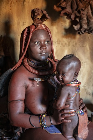 Himba woman sitting with baby in traditional hut, Himba village, Kaokoveld, Kunene, Namibia