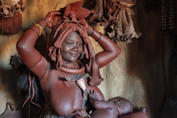 Himba woman sitting with baby in traditional hut, Himba village, Kaokoveld, Kunene, Namibia