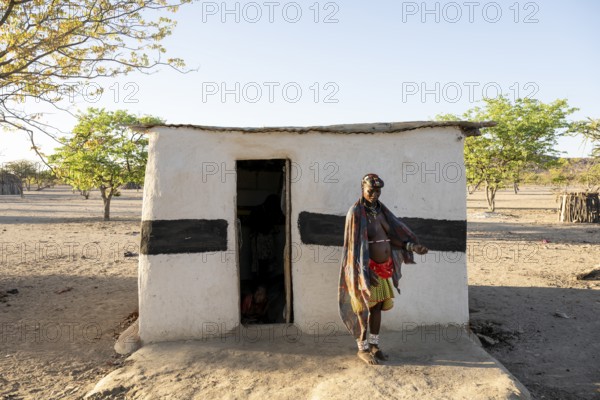 Woman in front of hut, village in the savanna, Hakaona tribe, also Havakona or Hakawona, near Opuwo, Kunene, Namibia