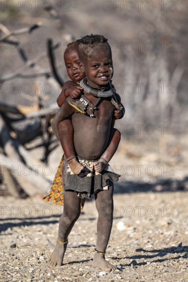 Himba child carrying baby piggyback, traditional Himba village, Kaokoveld, Kunene, Namibia