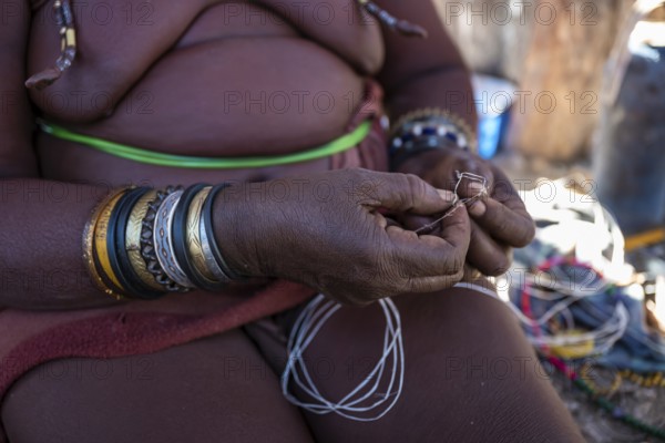 Himba woman doing handiwork, making hand bands for tourists, traditional Himba village, Kaokoveld, Kunene, Namibia