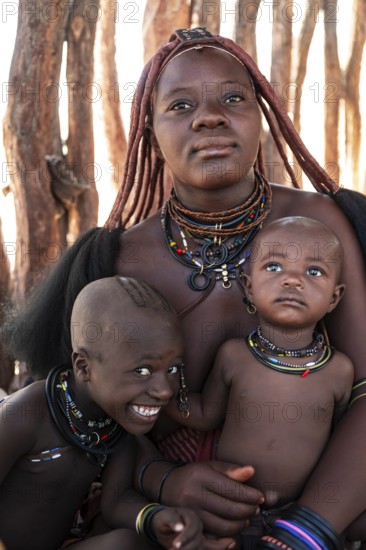 Himba woman with baby and grinning child, traditional Himba village, Kaokoveld, Kunene, Namibia