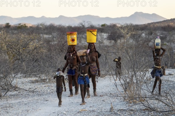 Himba woman and children run to fetch water with canisters through dry countryside, traditional Himba, Kaokoveld, Kunene, Namibia