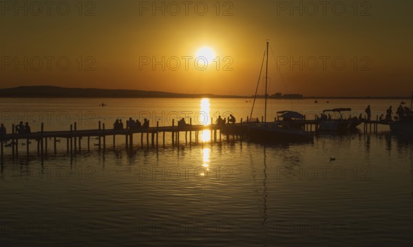 Sunset over the Steinhuder Meer with people on a pier, reflecting sailboats, peaceful, Steinhude