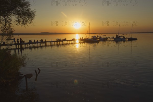 Sunset on Lake Steinhude with people on a jetty and sailboats, relaxed atmosphere, Steinhude