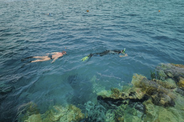 Two snorkelers snorkeling at water surface sea surface of the Red Sea, left man without sun protection in front of it person with thin wetsuit protects against intense sunlight sunburn, Red Sea, Egypt