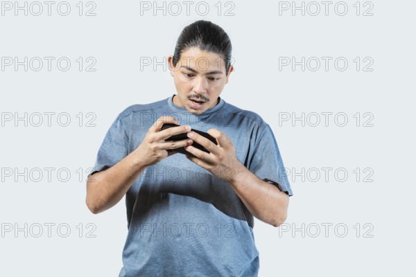Surprised young man playing with cell phone isolated. Amazed gamer playing with cell phone isolated