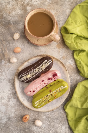 Glazed Eclairs on brown concrete background and green linen textile, cup of coffee, top view, flat lay, close up