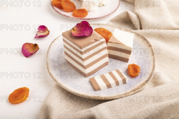 Cocoa and milk jelly with dried apricots on white wooden background and linen textile, side view, close up, minimalism