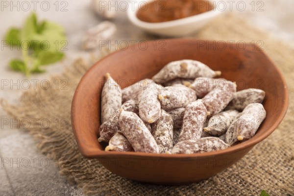 Small smoked Chicken sausages in clay bowl on brown concrete background and linen textile. side view, close up, selective focus
