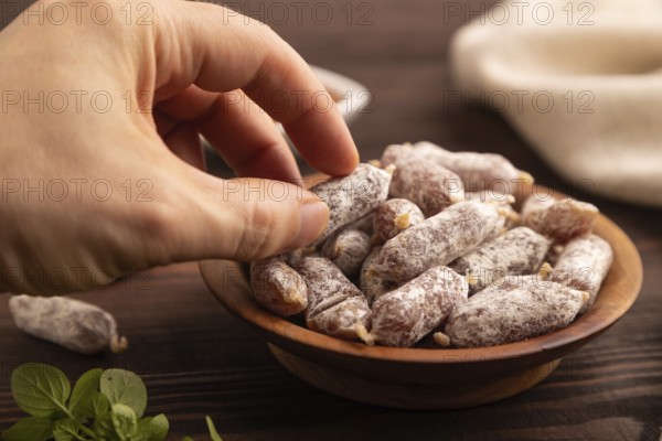 Small smoked Chicken sausages in wooden bowl with hand on brown wooden background and linen textile. side view, close up, selective focus