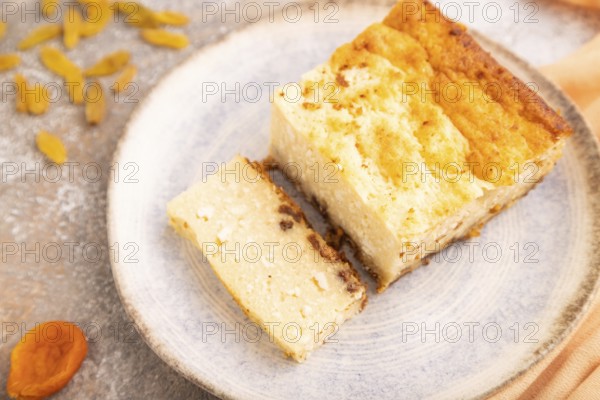 ?ottage cheese ?asserole, Curd cake, with dried apricots and raisins on brown concrete background and orange textile, side view, selective focus, minimalism