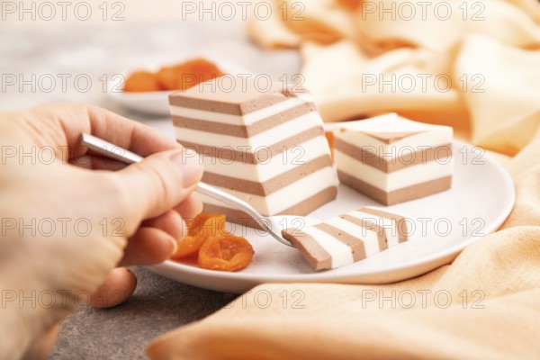Cocoa and milk jelly with dried apricots with hand on brown concrete background and orange textile, side view, close up, selective focus, minimalism