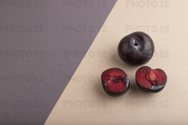 Purple Plum Cut in half on beige and gray pastel paper background. Side view, copy space. healthy food, vegetable, minimalism