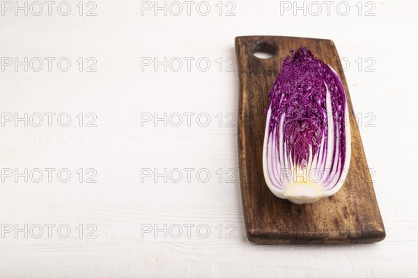 Purple Chinese cabbage on cutting board on white wooden background, side view, copy space, minimalism