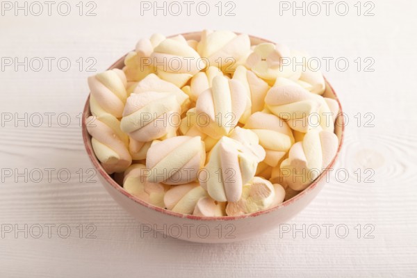 Orange and pink marshmallow in ceramic bowl on white wooden background, side view, copy space, minimalism