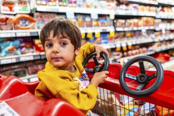 Adorable toddler having fun driving a shopping cart with a toy steering wheel attached, enjoying a family grocery shopping trip in a brightly lit supermarket