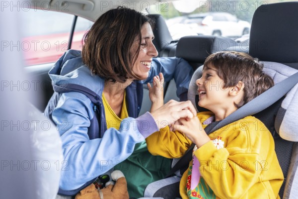 Mother turning back to her son, sitting in a child car seat, sharing joyful moments and laughter during a delightful car trip, strengthening their bond through love and togetherness