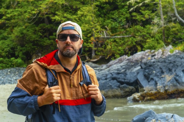 Male tourist wearing sunglasses and a baseball cap enjoying the stunning beaches of tofino, a renowned travel destination on vancouver island, british columbia