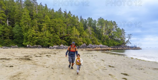 Father and son running together on a sandy beach with lush green forest and rocky coastline in tofino, vancouver island, british columbia, canada, enjoying quality family time in nature
