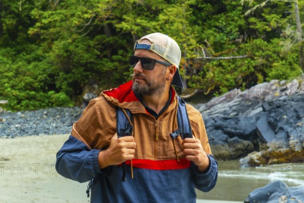 Male tourist wearing sunglasses and a baseball cap, exploring the beautiful beaches and lush rainforests of tofino, a popular travel destination on vancouver island, british columbia, canada
