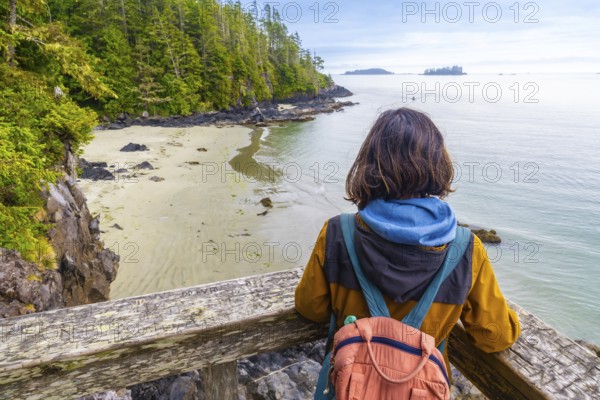 Tourist with a backpack is enjoying a breathtaking view of the ocean and coastline from a wooden viewpoint in tofino, a popular destination on vancouver island, british columbia, canada