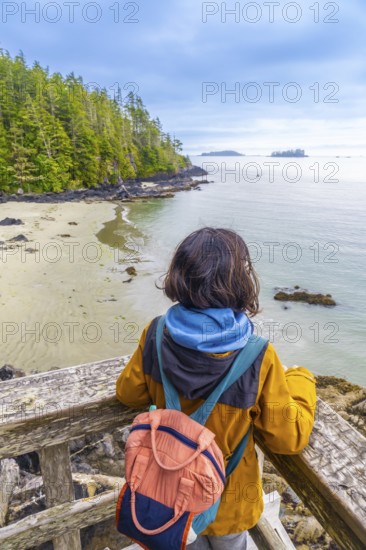 Tourist with a backpack is enjoying a breathtaking view of the ocean and coastline from a wooden viewpoint in tofino, located on vancouver island, canada