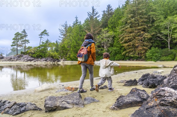Mother and son walking along the shore of mackenzie beach in tofino, enjoying the breathtaking natural beauty of vancouver island on a cloudy summer day