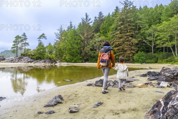 Mother and daughter, hand in hand, enjoy a peaceful stroll along mackenzie beach in tofino, british columbia, surrounded by the serene beauty of vancouver island's lush rainforest and calm waters