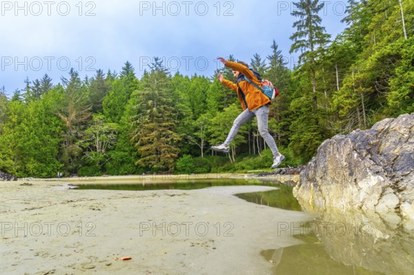 Energetic backpacker leaping across a tide pool on mackenzie beach in tofino, showcasing the beautiful natural scenery of vancouver island, british columbia