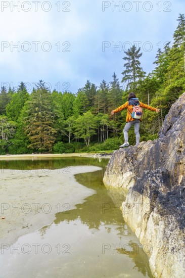 Female hiker standing on rock with open arms, enjoying the serene view of the inlet and lush forest in tofino, a popular tourist destination on vancouver island, british columbia, canada