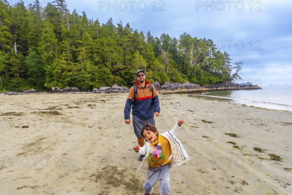Father and son are walking on chesterman beach in tofino, british columbia, canada, enjoying the sunny weather and breathtaking scenery of the pacific ocean and lush rainforest