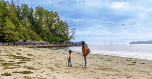 Tourists enjoying a leisurely walk along mackenzie beach in tofino, admiring the breathtaking scenery of vancouver island's coastline and lush vegetation