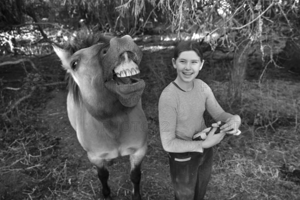 Laughing young girl next to her whining horse, black and white, Othenstorf. Mecklenburg-Vorpommern, Germany