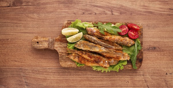 Fried crispy red mullet fish, on a wooden chopping board, with lime, no people