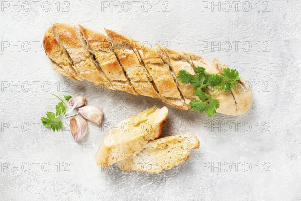 Garlic bread, baguette with garlic butter and herbs, on a light table, top view
