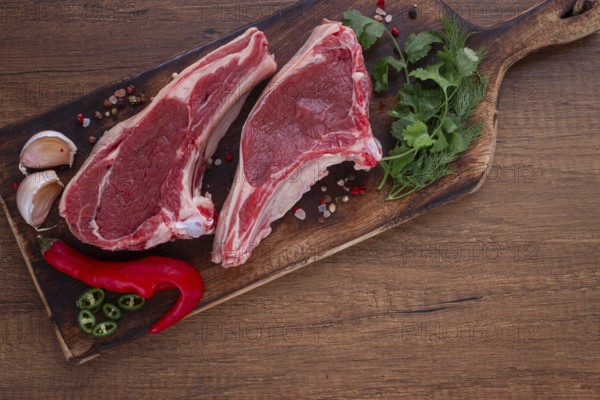 Freshly sliced lamb chops, with herbs and vegetables, on a wooden board, ready to cook, on a wooden table