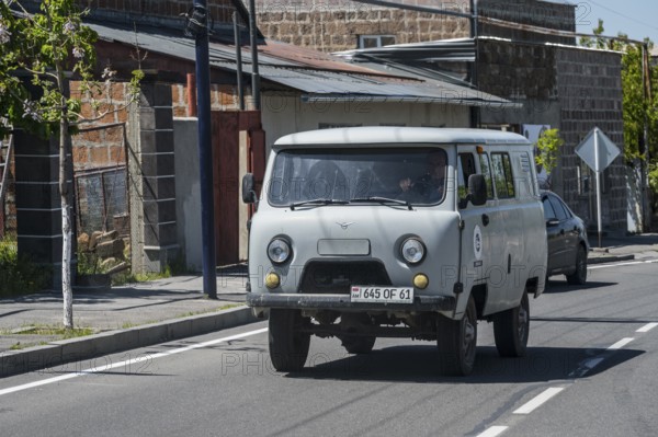 White pickup truck drives past old buildings on a quiet street, UAZ Buchanka, Armenia