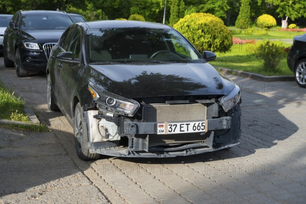 Black Kia parked in a green parking environment with front damage, Armenia