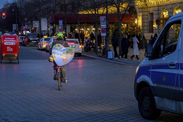 Grandma for Future is cycling back after the Fridays for Future rally. On the left, bicycle rickshaw with the inscription: Discover activities in Berlin, on the right, police personnel carrier. Berlin, 12.12.2025