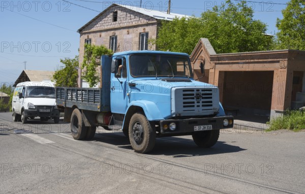 A light blue truck on a village road in front of a building under clear sky, ZIL-4331 truck powered by gas, Armenia