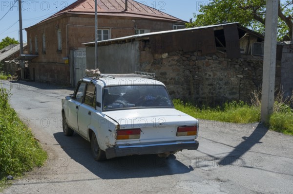 A rear view of an old car on a rural road surrounded by old buildings, Lada 2107, also WAS-2107, VAZ-2107, Lada Nova or Lada Riva drives without a license plate, Armenia