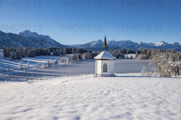 Snowy chapel with mountain backdrop and clear sky, surrounded by forests, Hegratsrieder See, near Füssen, Ostallgäu, Allgäu, Bavaria, Germany