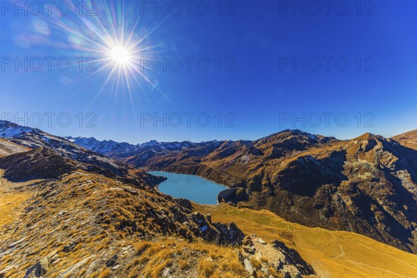 The sun shines over the mountains of the Val d'Anniviers, below the dam and the turquoise Lac de Moiry reservoir, Valais Alps, Canton of Valais, Switzerland