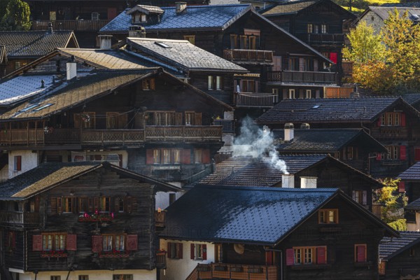 Smoke rises over the roofs of old wooden houses in Vissoie, Val d'Anniviers, Valais Alps, Canton of Valais, Switzerland