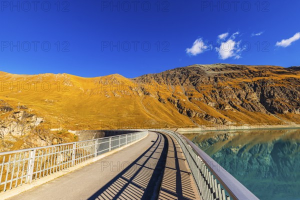The dam of the Lac de Moiry reservoir, behind alpine meadows in autumn colors, Val d'Anniviers, Valais Alps, Canton of Valais, Switzerland