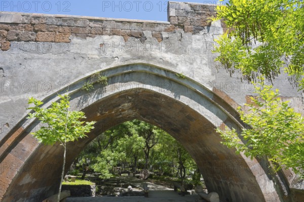 View of an old stone bridge structure against a wooded background on a sunny day, part of a three-arched bridge over the Kassagh from 1664, Ashtarak, Aštarak, Aragazotn province, Armenia