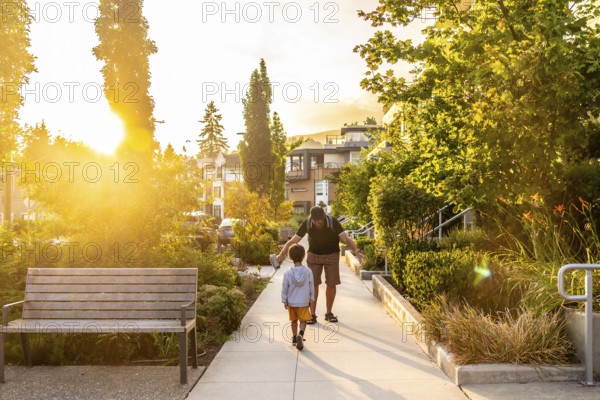 Father and son enjoying a leisurely stroll along a tree lined residential street in vancouver. British columbia. Bathed in the warm glow of the setting sun. Creating a peaceful and heartwarming scene