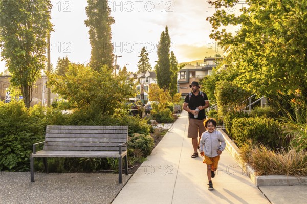 Father and son are enjoying a leisurely walk through a tree lined residential street in vancouver, british columbia, with the setting sun casting a warm glow on the scene